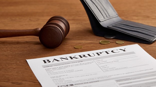 bankruptcy paperwork sits in front of a gavel and a wallet with a few coins coming out of it