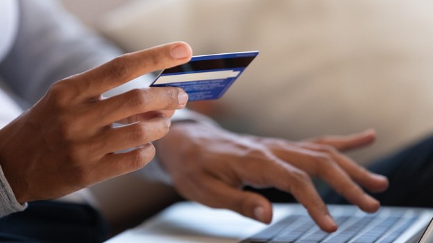 a person holds a credit card in front of their laptop computer as they perform a credit card balance transfer