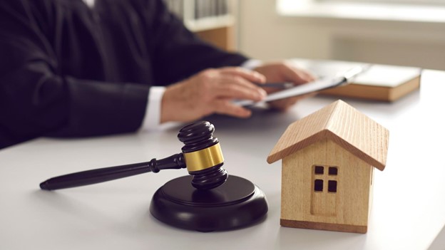 a gavel sits next to a small wooden house model in front of a foreclosure attorney