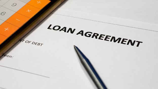 a pen and calculator sit on top of a loan agreement