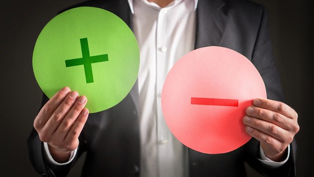 a person holds up a green plus sign and a red minus sign to represent the pros and cons of debt consolidation