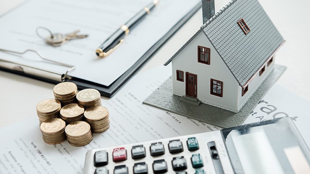 a house model sits next to coins and a calculator