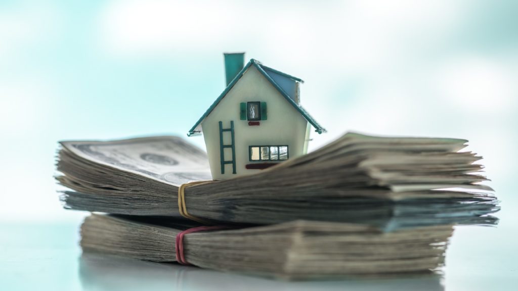 a house model sits on top of piles of cash