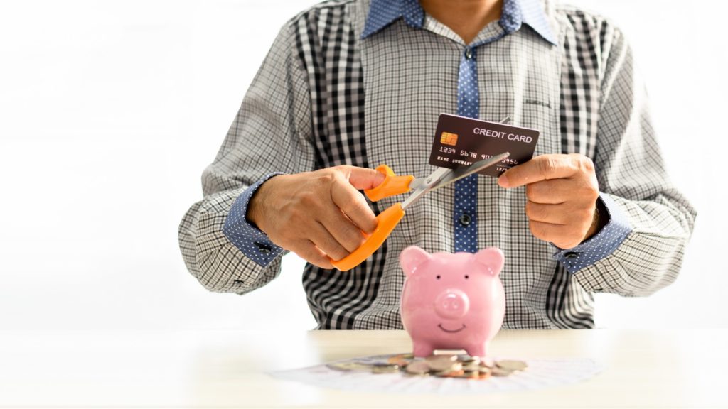 a man cuts a credit card with scissors over a piggy bank