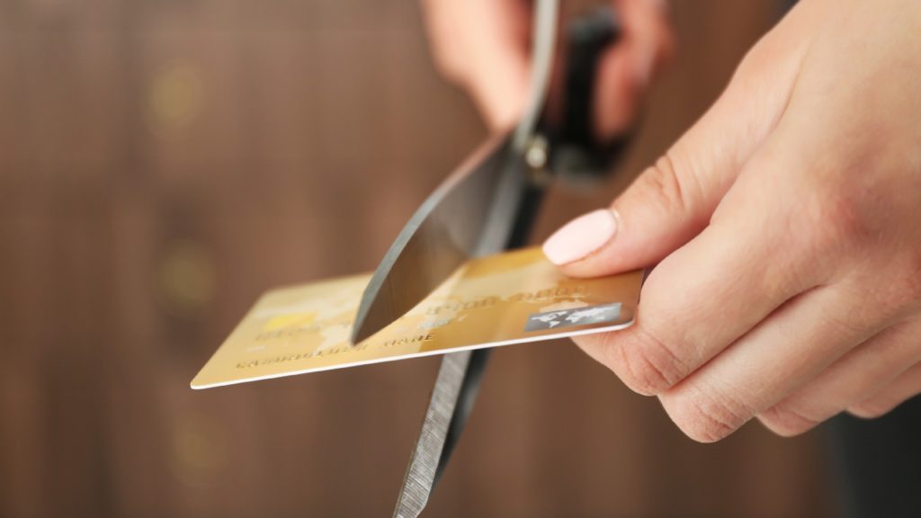 a person cuts a credit card with scissors, which is a way you can prevent your credit score from dropping after divorce