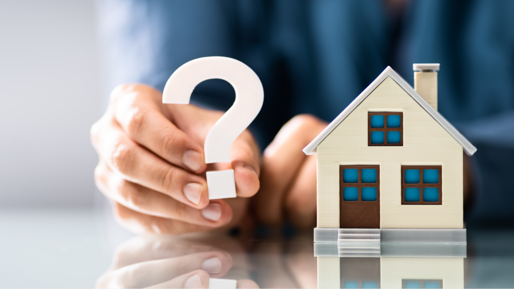 a person holds a model question mark next to a model house