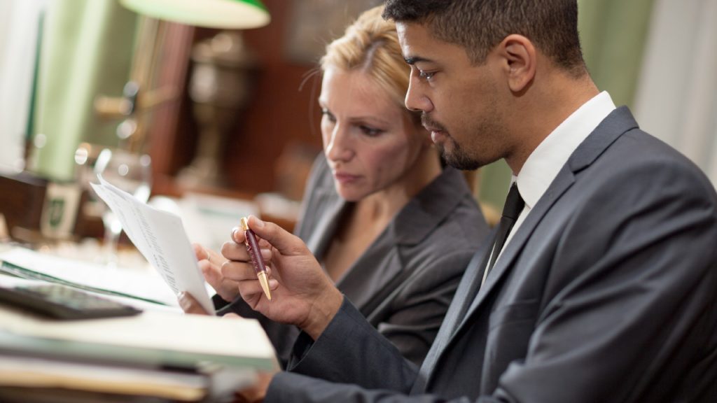 two lawyers talk about paperwork at a desk