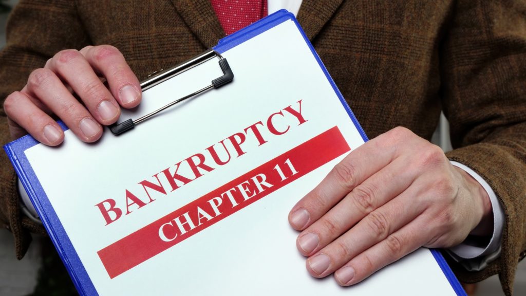 a person wearing a suit and tie is holding a clipboard with papers labeled Bankruptcy Chapter 11