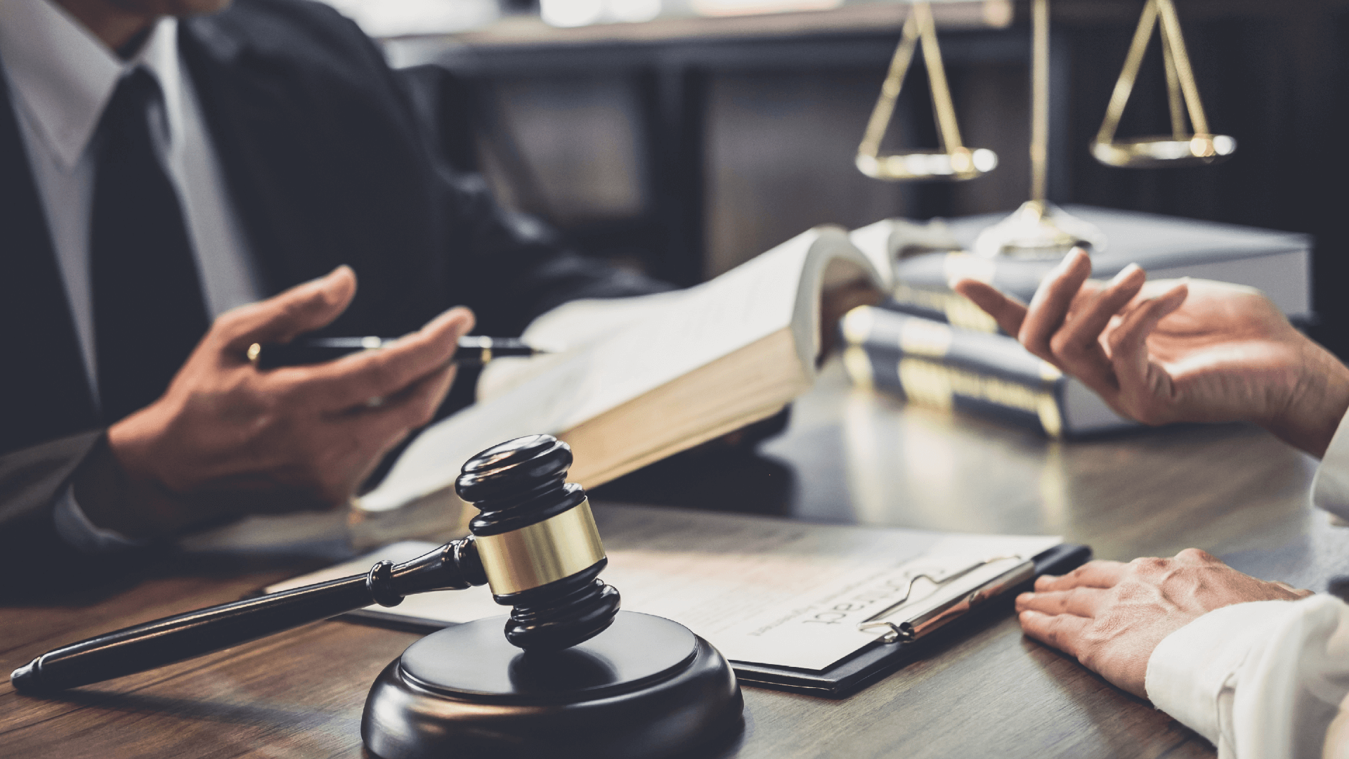 lawyer reviewing case with client on desk with gavel, justice scales and law books on display