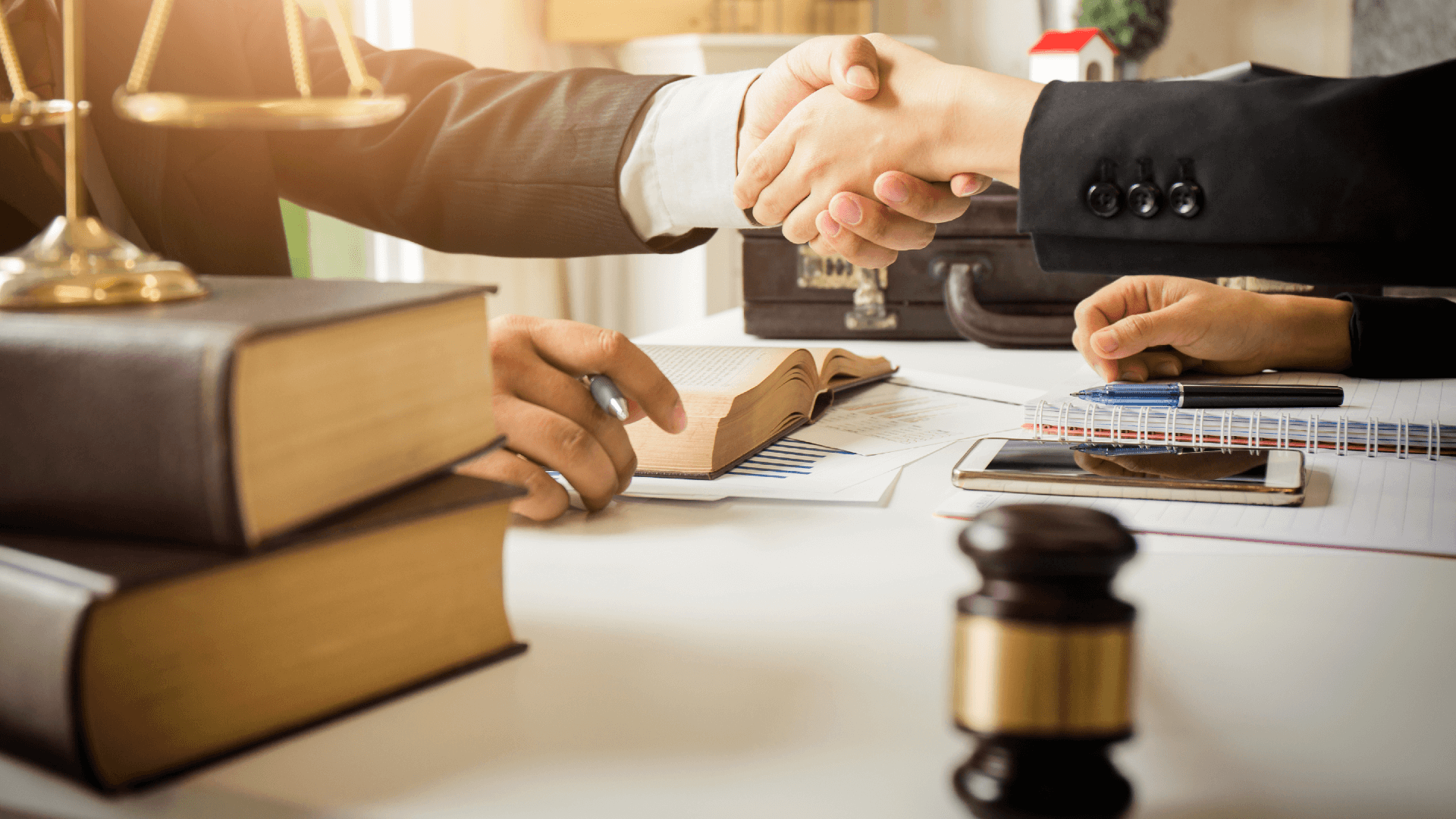 men in suits shake hands on desk with gavel justice scales and law books on display