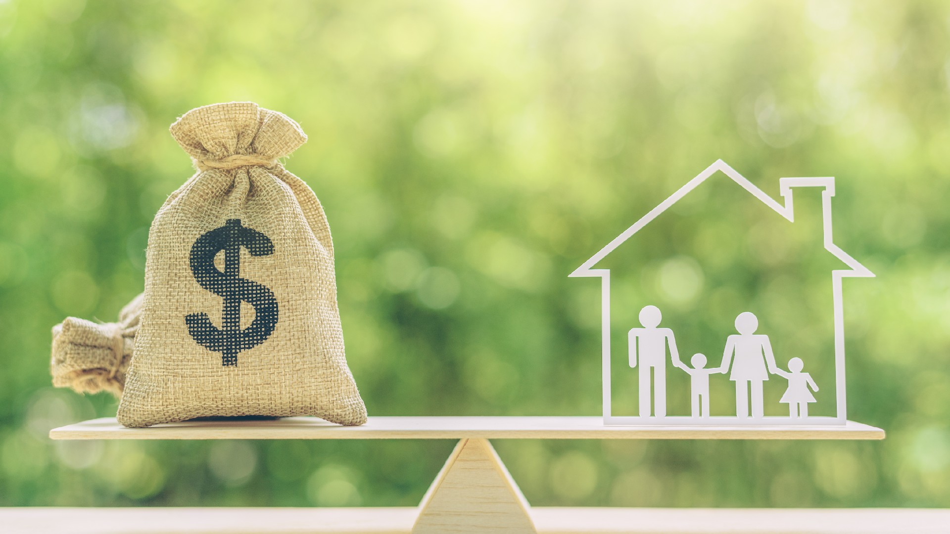 A bag of money sits on a seesaw with a house diagram to represent financial security