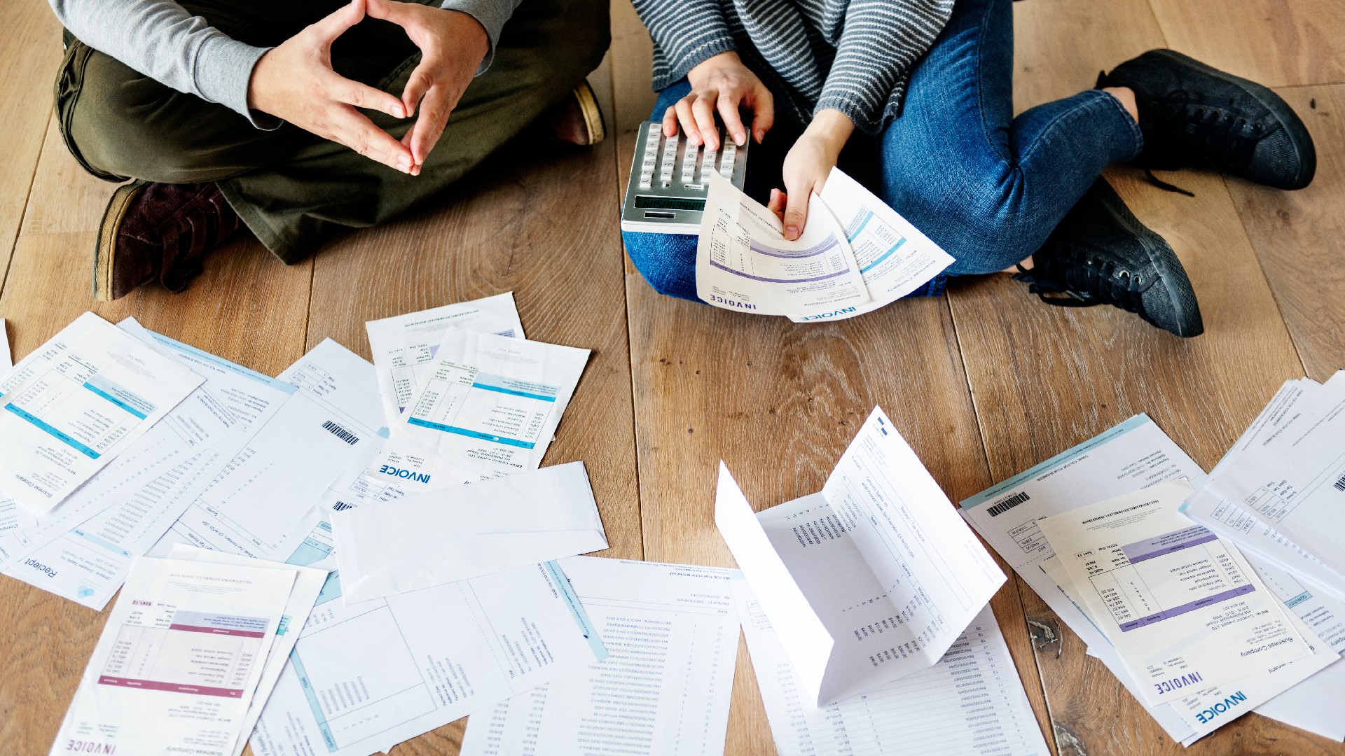 A couple manages debt while sitting on the floor with papers and a calculator and probably wondering whether lawsuits and judgements are viable options