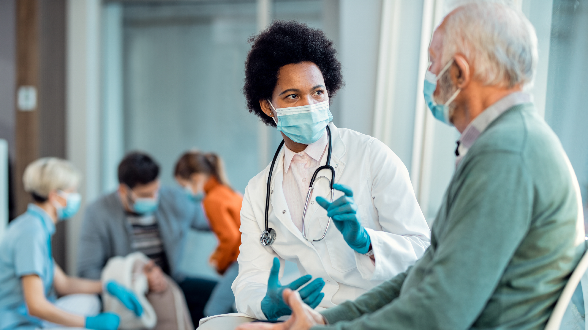 A doctor speaking to a patient in the waiting room and they are both wearing masks