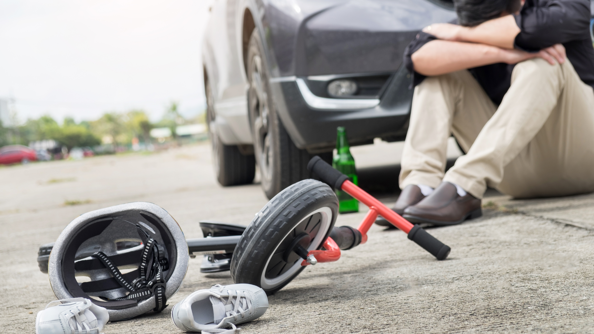 A fallen bike lies in front of a car as the driver puts their head in their arms in sadness