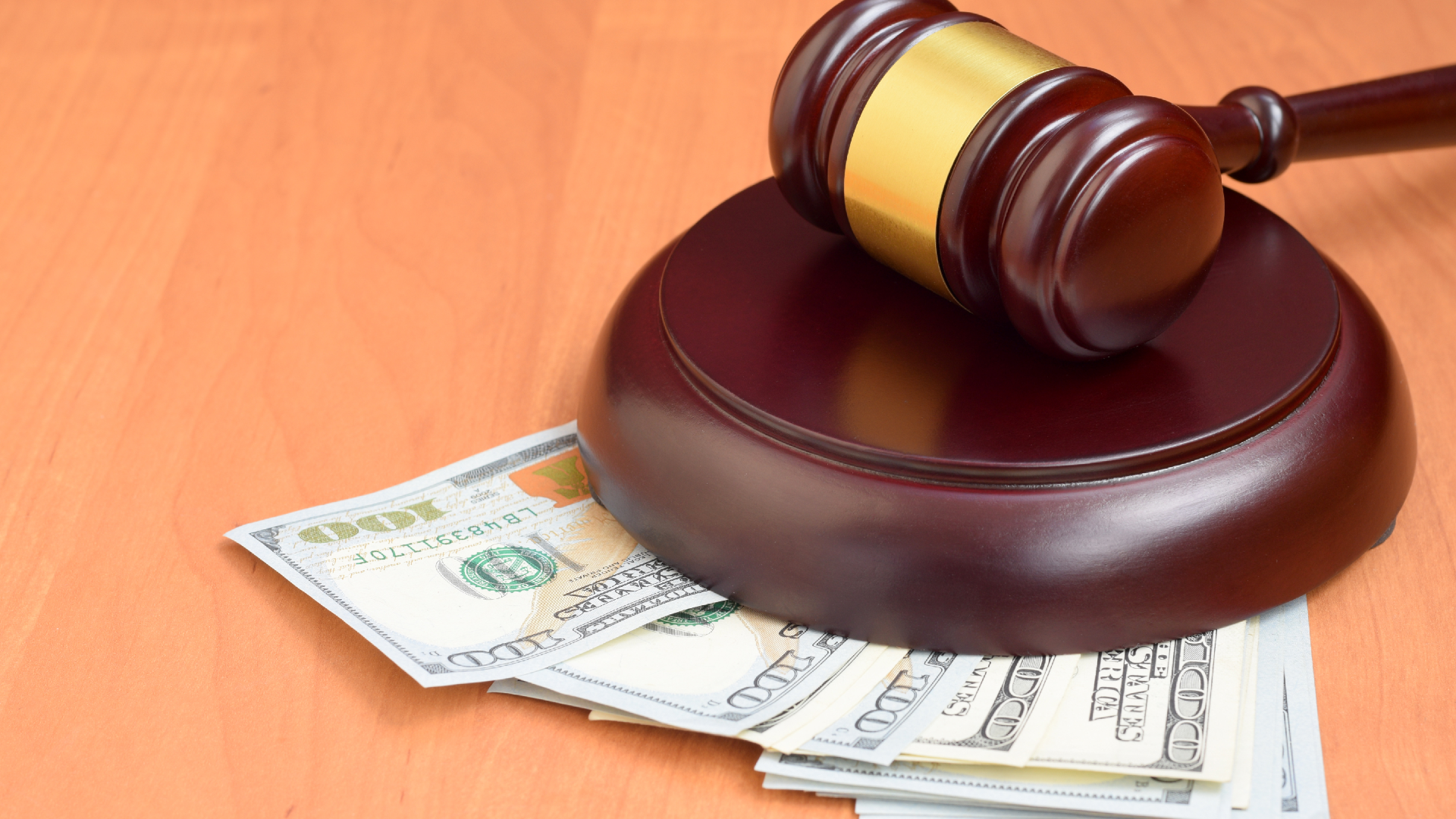 A judge’s gavel sits on top of a pile of $100 bills
