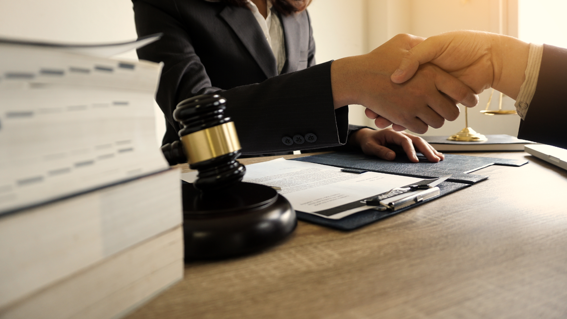 A lawyer shaking hands with their client next to a gavel and some law books