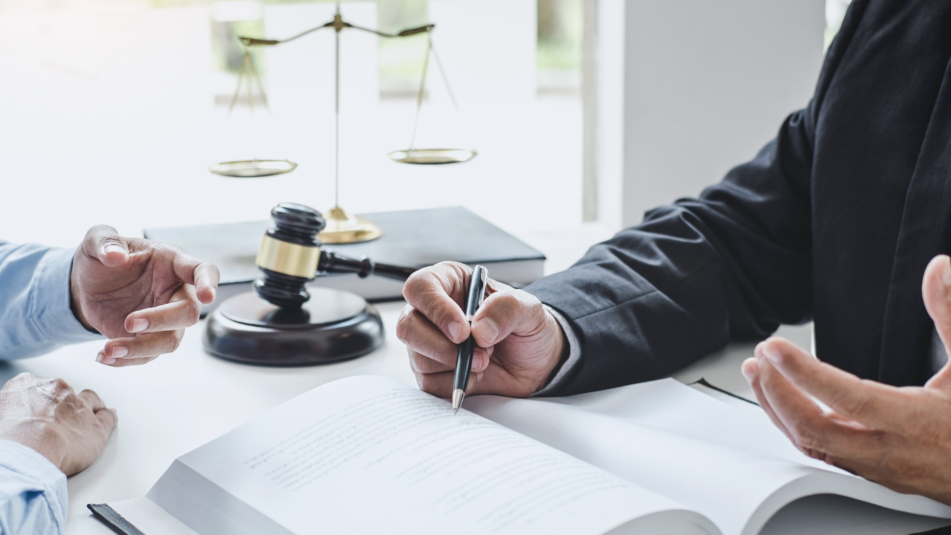 A lawyer speaking with their client as they point to a book next to a gavel and scales of justice