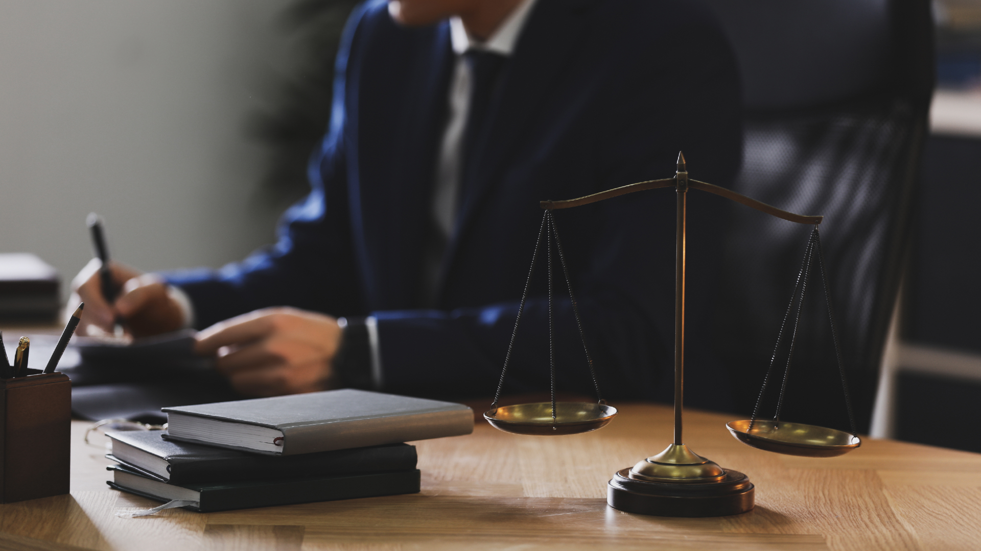 A lawyer takes notes on their desk next to a small model of the scales of justice