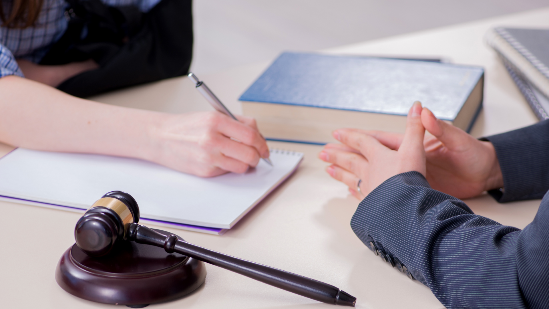 A lawyer taking notes on a desk with a law book and a gavel lying on top of it