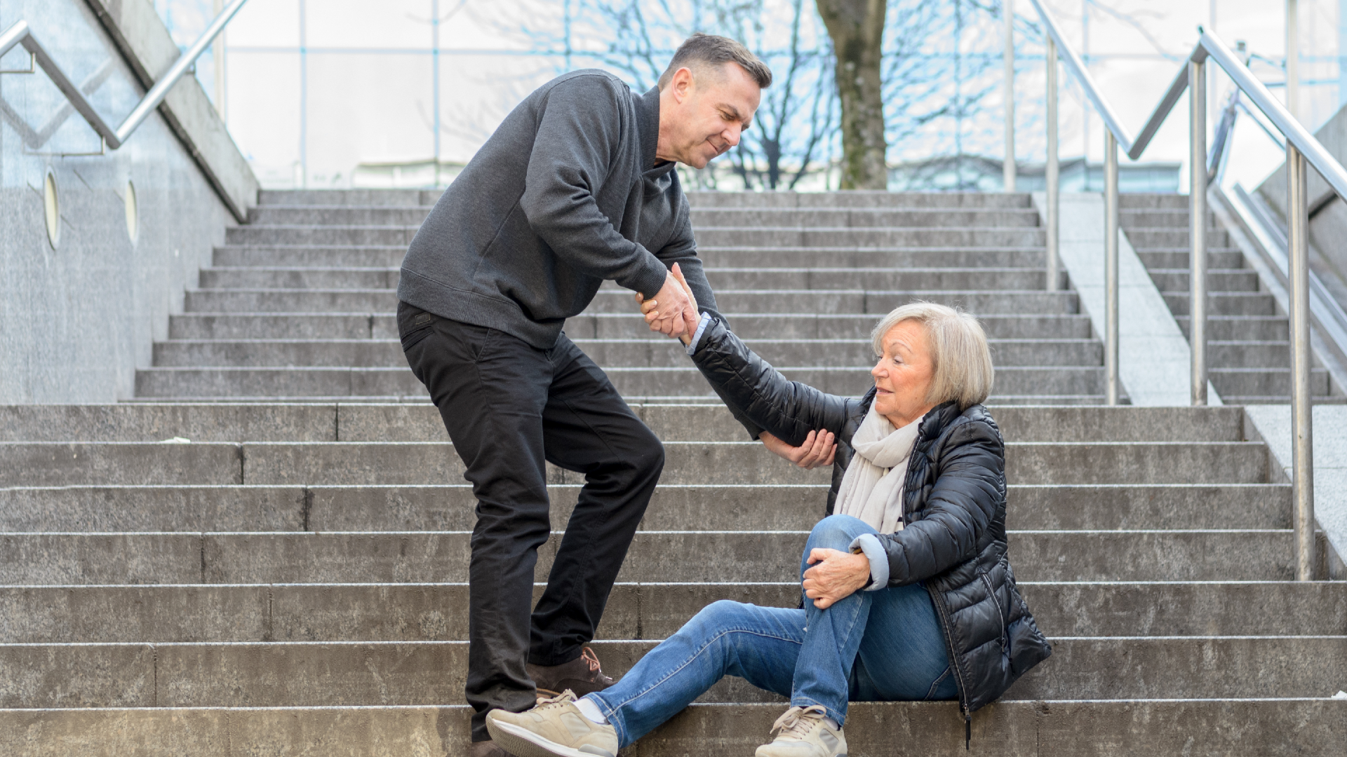 A man helping a woman up after a slip and fall on outdoor stairs