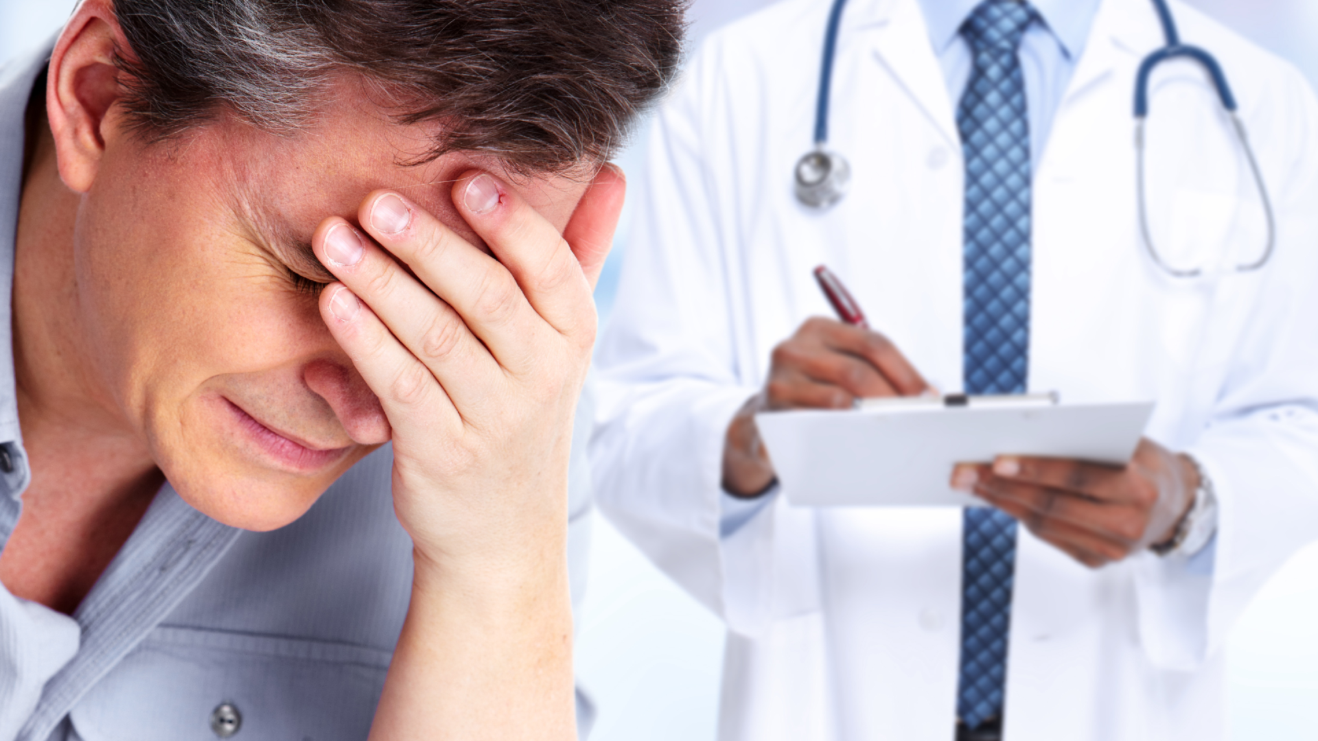 A man holds his head as a doctor writes notes on the paperwork behind him