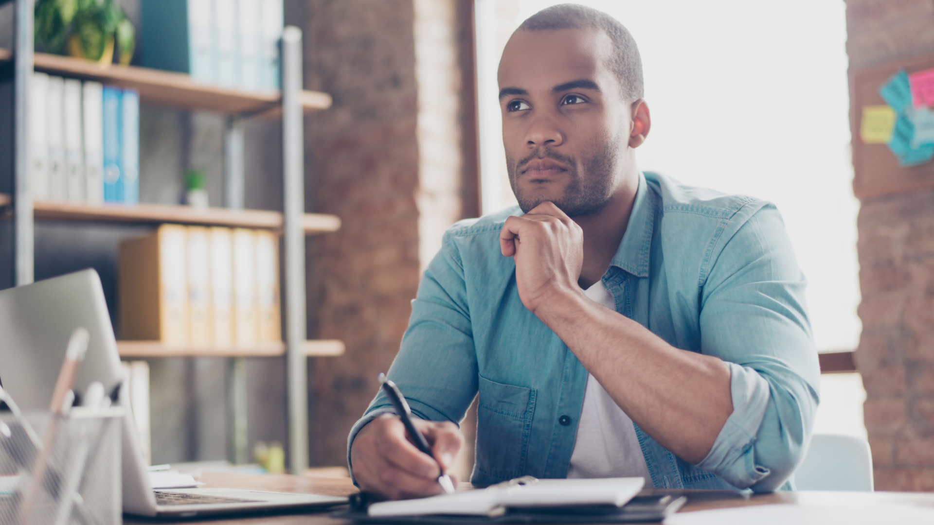 A man sitting at desk thinking while writing notes in his 