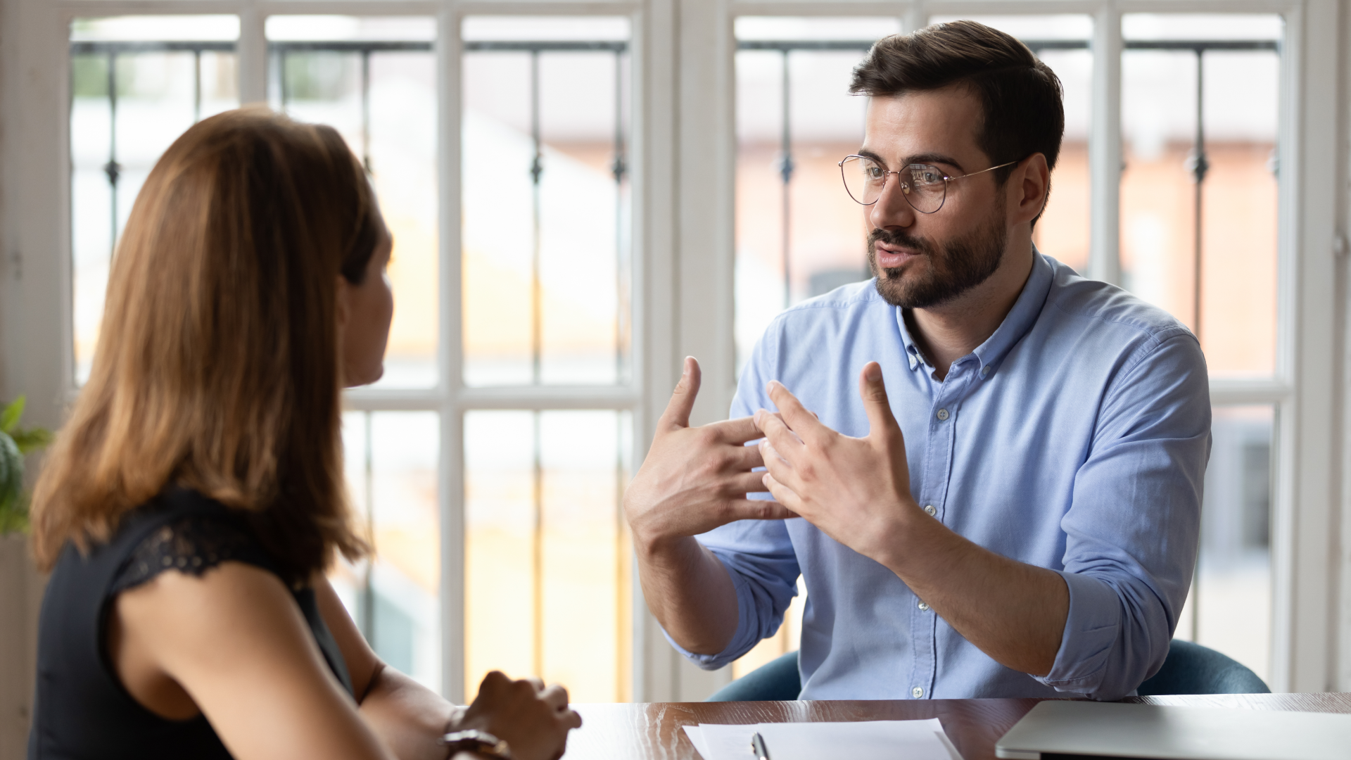 A man wearing glasses talking to a woman at her desk