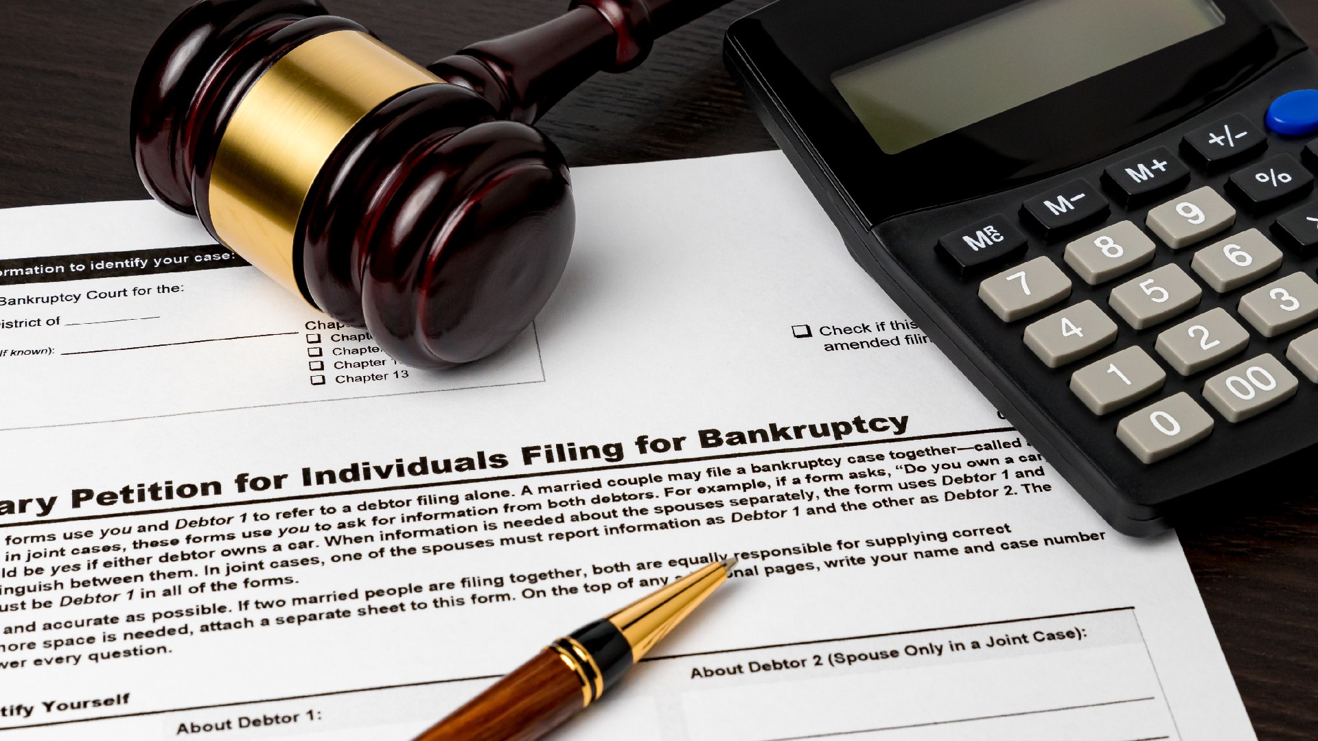 A gavel, calculator, and a pen sit on top of a petition filing for bankruptcy
