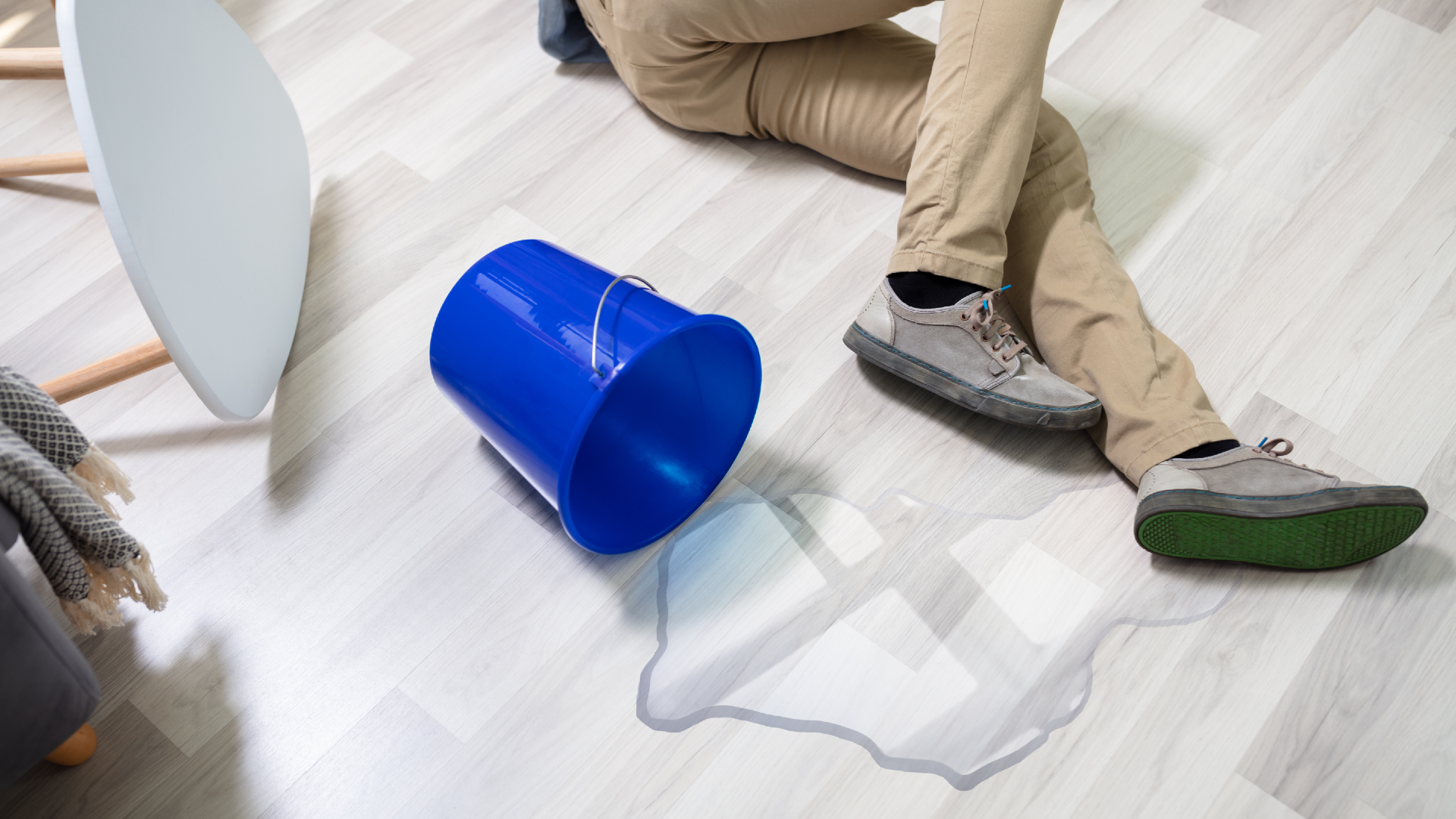A slip-and-fall accident where a person is lying on the floor next to a spilled bucket