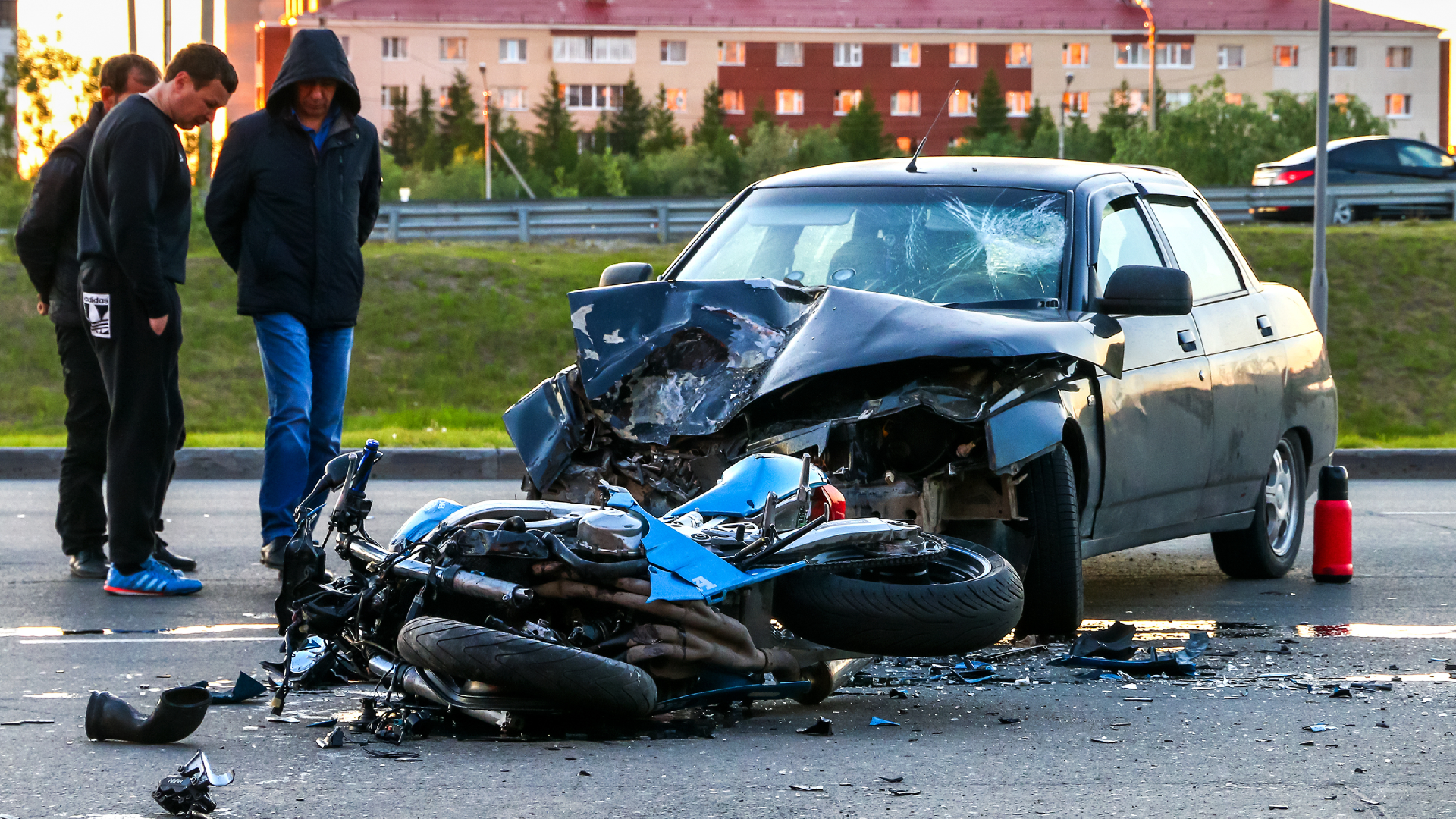 Three observers looking at motorcycle accident with destroyed motorcycle and car