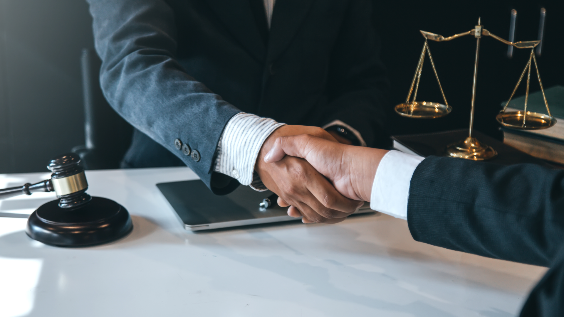 Two men in suits shaking hands by a gavel and justice scales