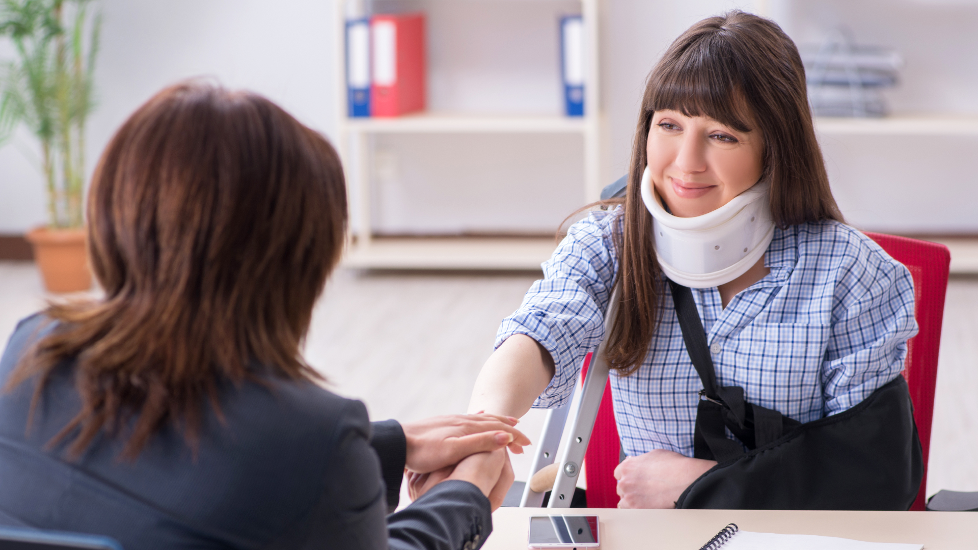 A woman wearing a neck brace and sling shakes hands with her lawyer